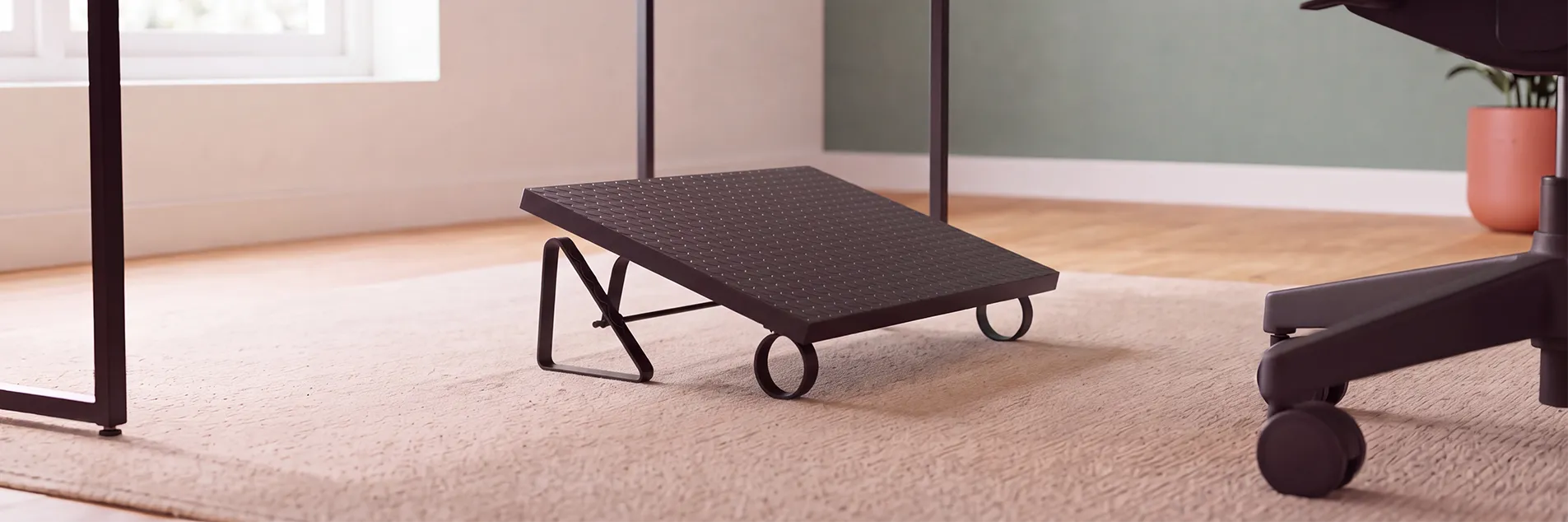 Apoio de pés ergonômico Robust posicionado embaixo da mesa de escritório e uma cadeira Comfy do lado direito da imagem.