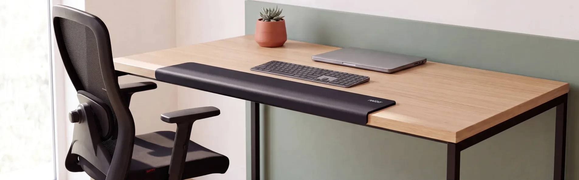Quebra quina de mesa preto em neoprene encaixado na borda frontal de uma mesa de madeira, com teclado e cadeira de escritório em home office.